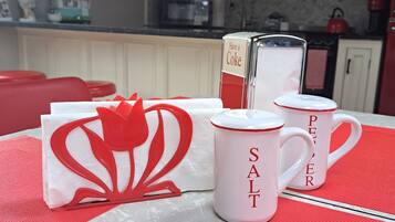 A kitchen with white cabinets, a microwave, and a red kettle. There are two white mugs with red text and a red and white decorative item on the table.