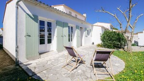 A white building with green shutters, a stone patio, and two folding chairs.