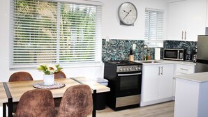 A modern kitchen with white cabinets, a black stove, a microwave, and a clock on the wall.