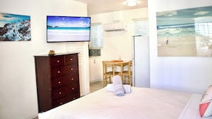 A bedroom with a bed, a dresser, a TV, a dining table with chairs, and a window with blinds. - Beachside studio steps from the sand (Hollywood)