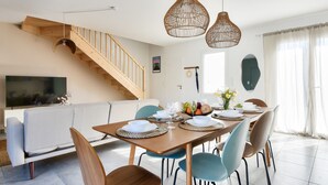 Een eetgedeelte met een houten tafel voor vier personen, omringd door stoelen, een trap en een televisie op de achtergrond.