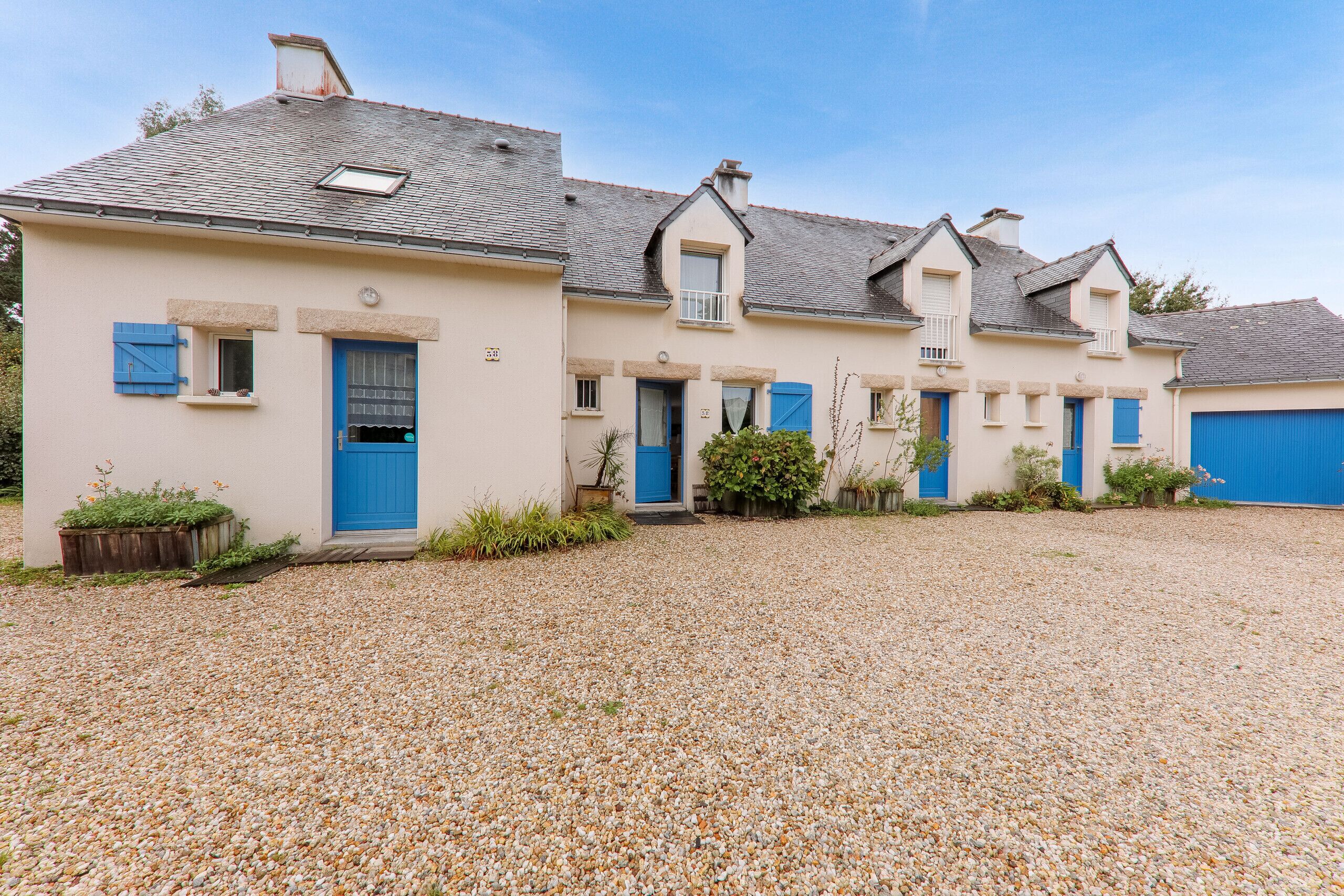 A row of three houses with blue doors and shutters, a gravel driveway, and a clear sky.
