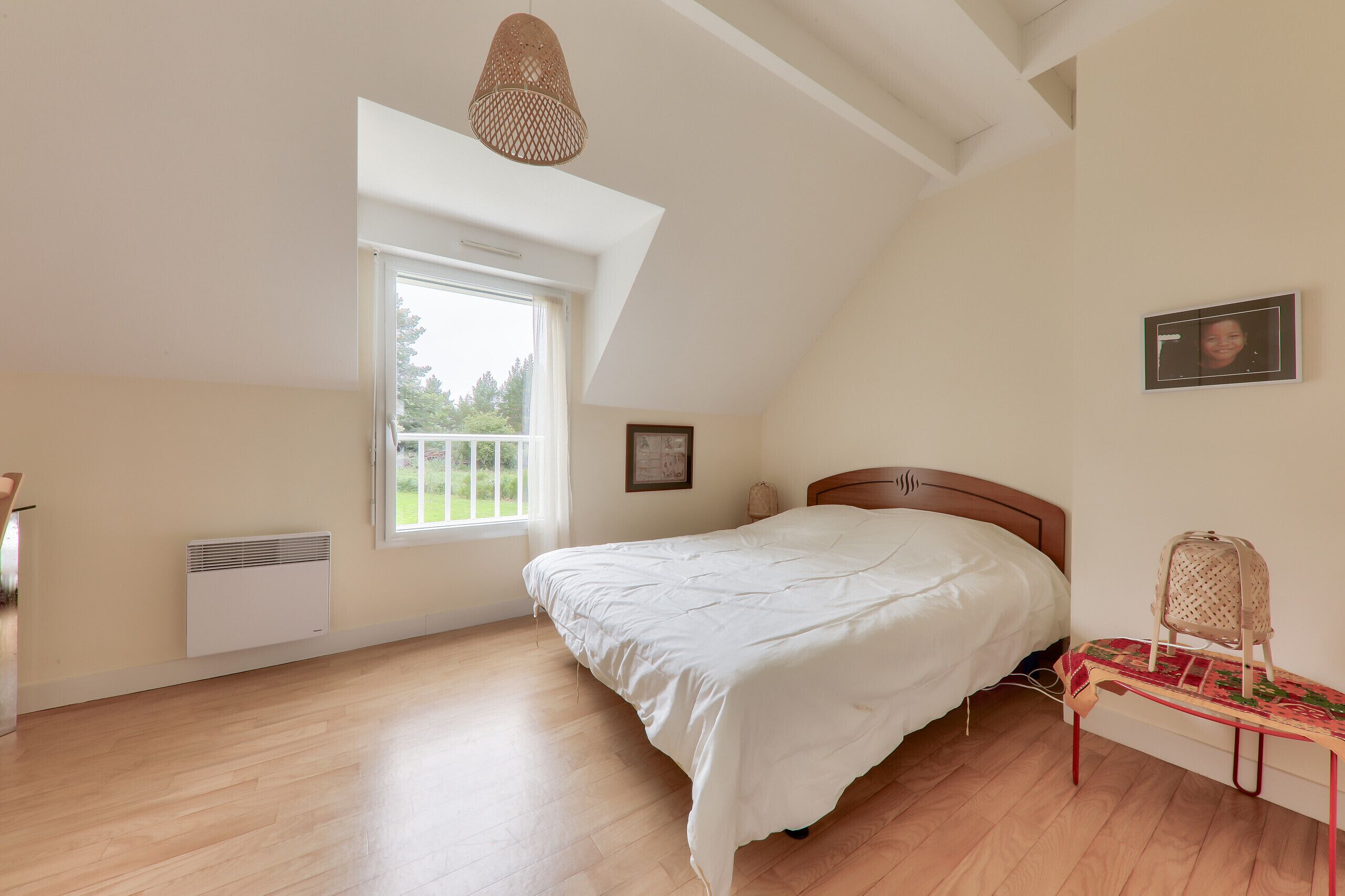 Un dormitorio con cama, ventana, radiador, lámpara colgante y una silla.