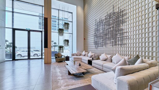 A spacious living area with a large window, a sectional sofa, a coffee table, and a decorative wall. - bnbme - Oxford Terraces - STUDIO (Dubai)