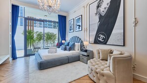 A modern bedroom with a large bed, a chaise lounge, and a view of the city. - bnbme - Oxford Terraces - STUDIO (Dubai)