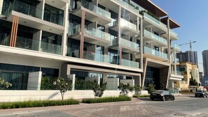 A multi-story building with balconies, a paved walkway, and a construction crane in the background. - bnbme - Oxford Terraces - STUDIO (Dubai)