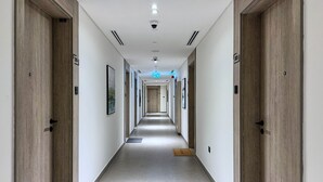 A long, narrow hotel corridor with wooden doors on both sides, numbered signs, and a blue exit sign. - bnbme - Oxford Terraces - STUDIO (Dubai)