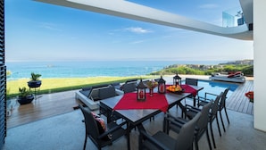 A modern outdoor dining area with a pool, overlooking a beach and the sea. - Boutique Ocean Views (Hermanus)
