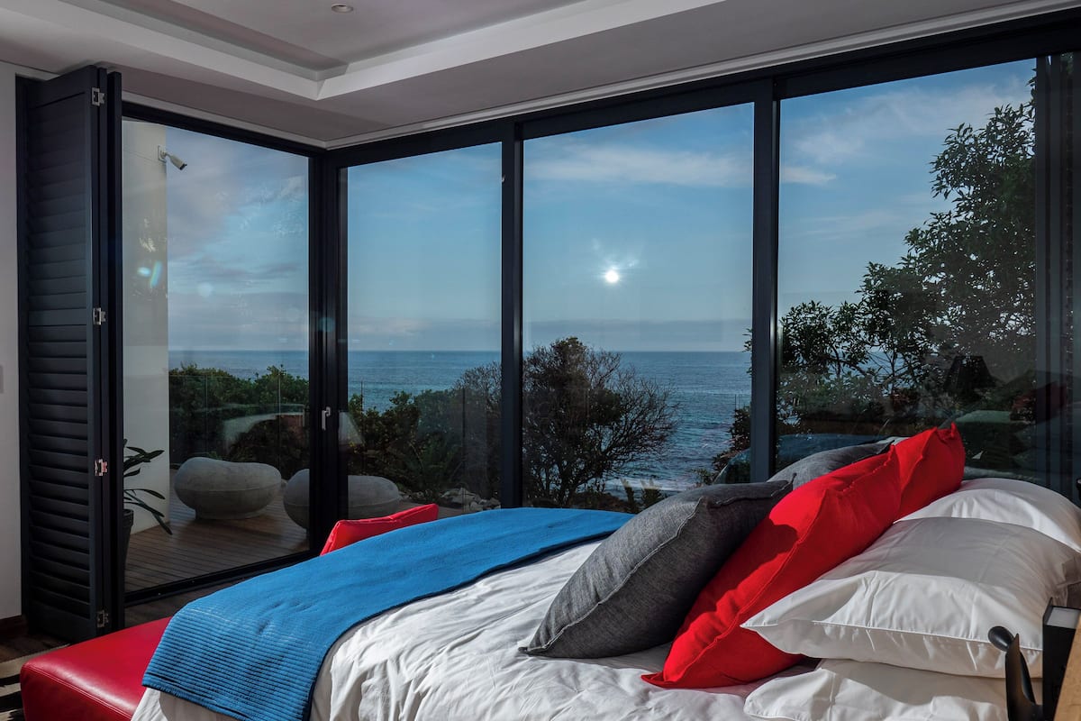A bedroom with a large sliding glass door leading to a balcony with a view of the sea.