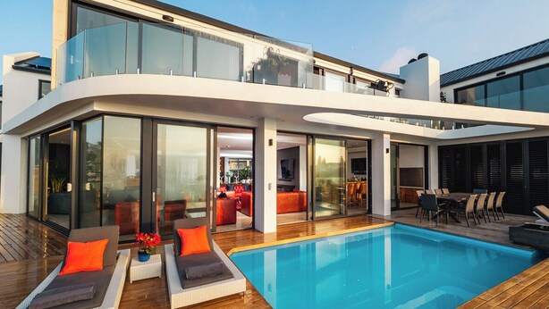 Ett modernt hus med en swimmingpool, utomhusmöbler och stora glasdörrar.