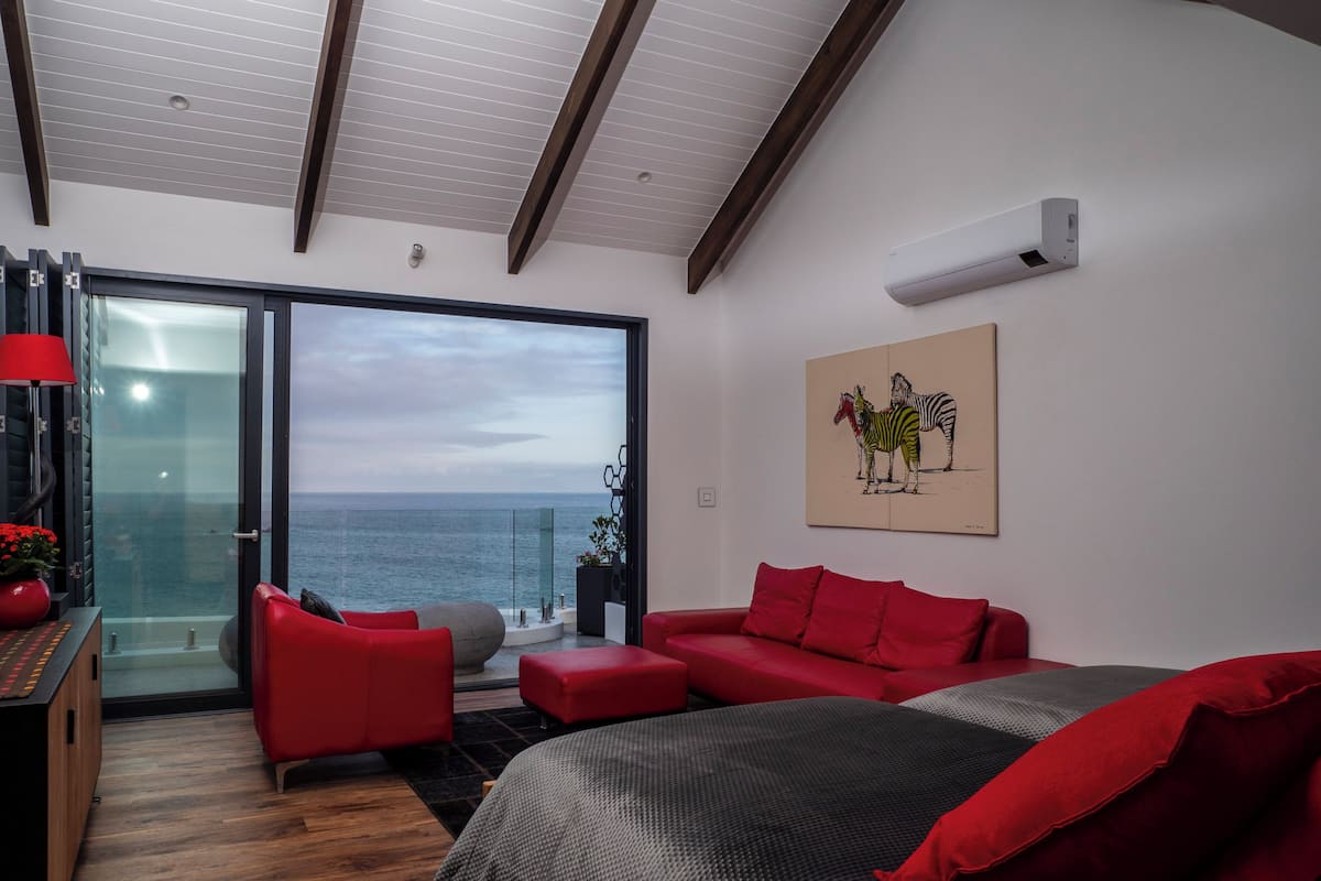 A modern bedroom with a large bed, red furniture, a glass door leading to a balcony, and a painting of zebras.