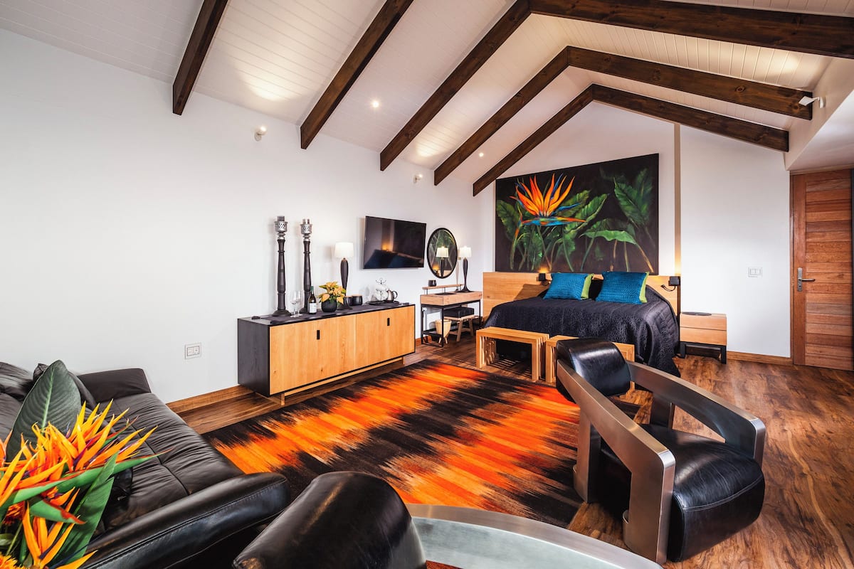 A modern bedroom with a large bed, a wooden headboard, a desk, and a sofa.