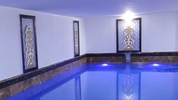 A large indoor swimming pool with clear blue water, surrounded by white walls with decorative panels. - Snowland Otel Sarikamis (Sarikamis)
