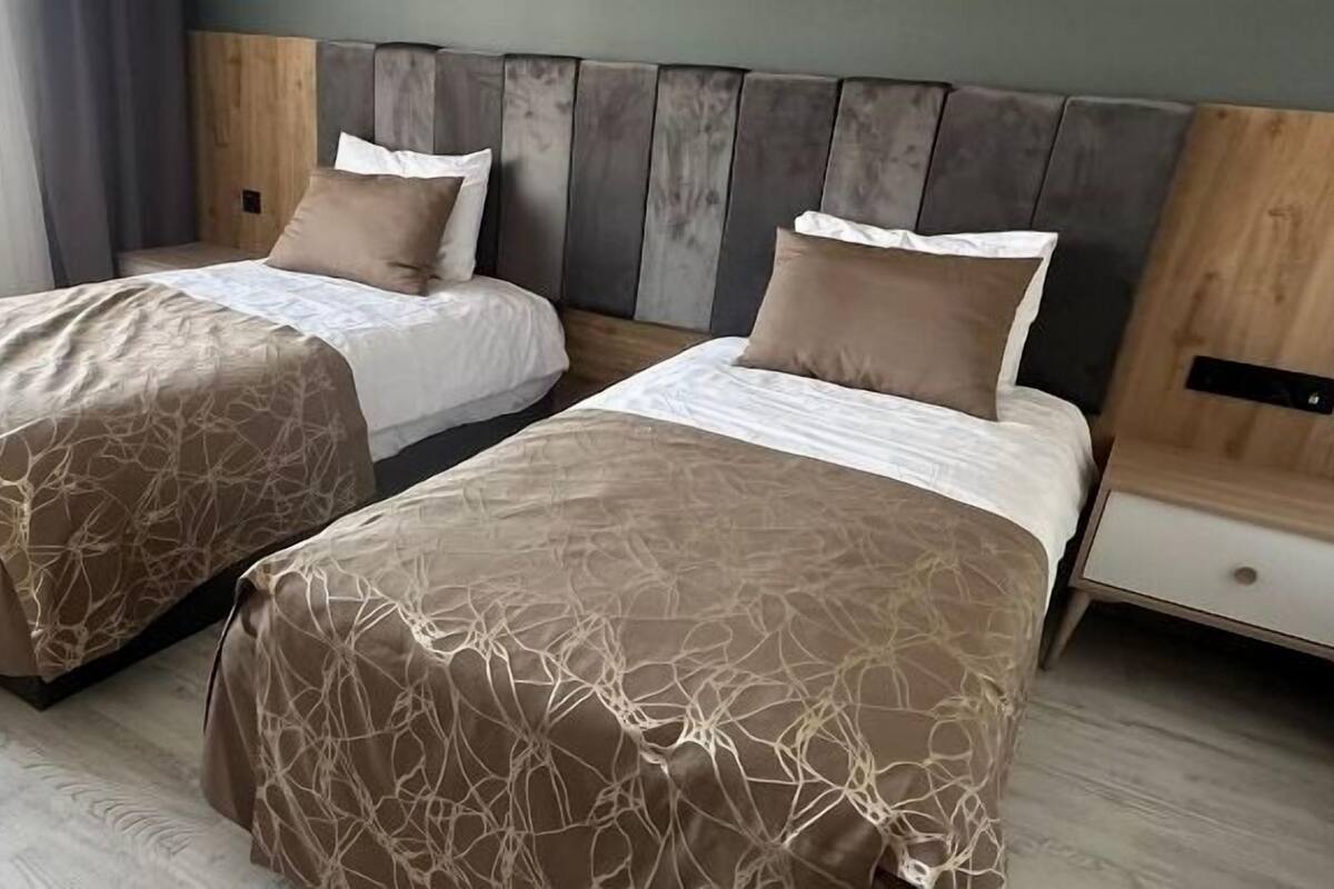 Due letti singoli con copripiumini a motivi marroni, una testiera in legno e un pavimento in legno chiaro.