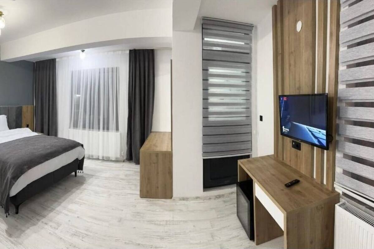 Una moderna camera d'albergo con un letto, una televisione, una scrivania e un'ampia finestra con tende.