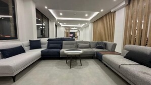 Ένα μοντέρνο σαλόνι με έναν αρθρωτό καναπέ, ένα στρογγυλό τραπεζάκι σαλονιού και μια τηλεόραση στο βάθος.