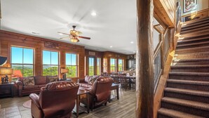 Un salon spacieux avec des canapés en cuir, des planchers en bois, de grandes fenêtres et un escalier.