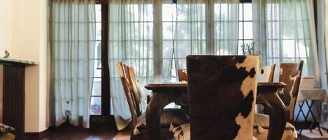 A dining area with a table and chairs, a red patterned rug, and a window with sheer curtains.