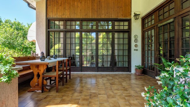 A patio with a wooden table and chairs, large sliding glass doors, and potted plants.