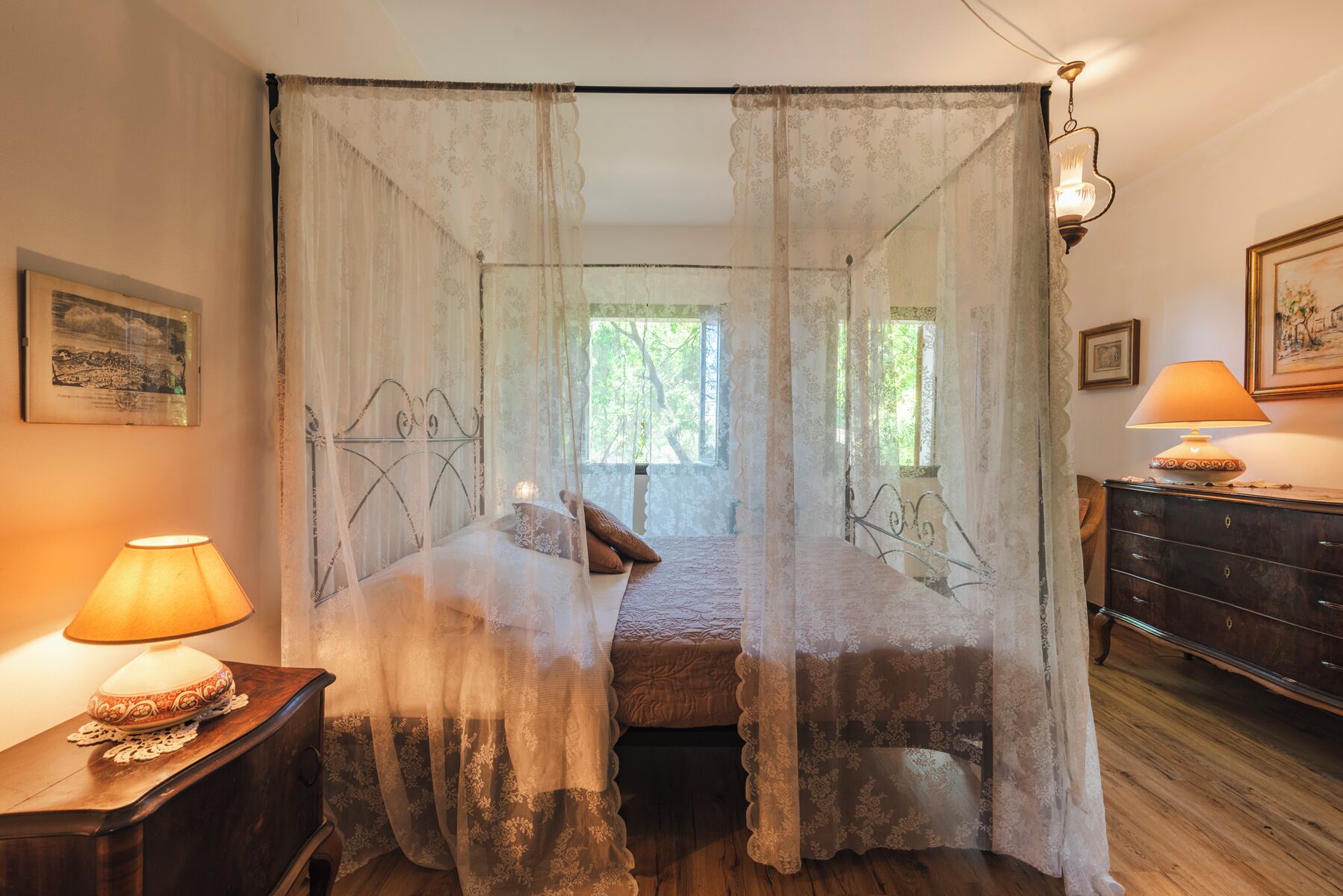 Une chambre à coucher avec un lit à baldaquin, une table de chevet avec une lampe, une commode et un tableau encadré au mur.