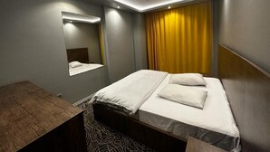Een moderne hotelkamer met een bed, een houten nachtkastje, een spiegel en een geel gordijn.