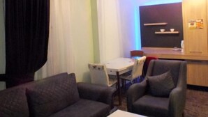 Een moderne woonkamer met een bank, fauteuil en een kleine tafel. Er is een televisie aan de muur en een keuken in de achtergrond.