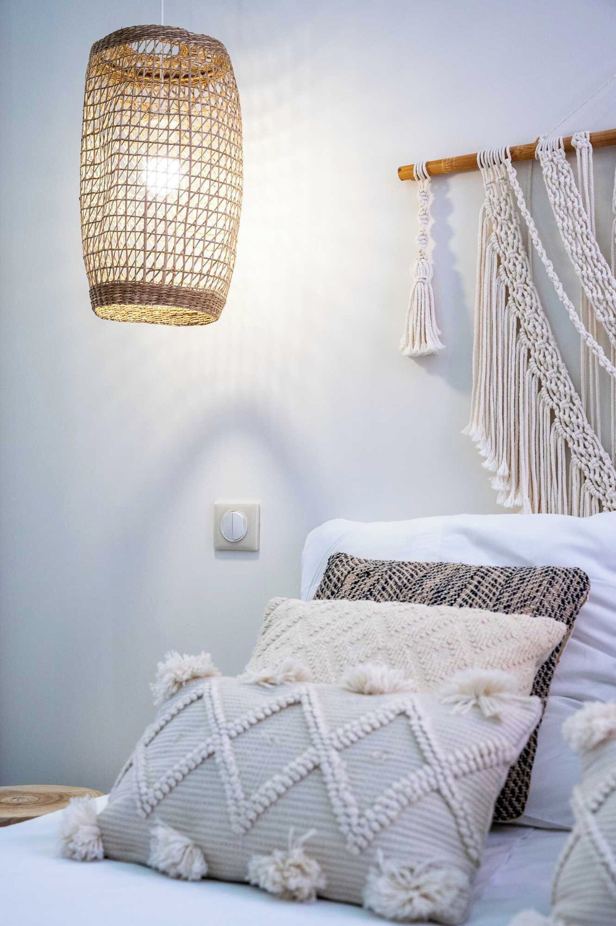 A room with a bed, macramé wall hanging, and a woven light fixture.