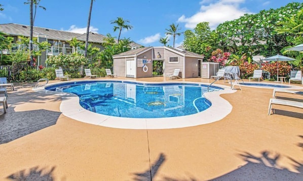 A swimming pool with lounge chairs and a small building, surrounded by tropical plants.
