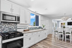 A modern kitchen with white cabinets, a stainless steel microwave, a gas stove, and a tiled backsplash.