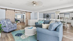 A spacious living area with a sofa, armchair, and coffee table, a kitchen in the background, and a sliding barn door.