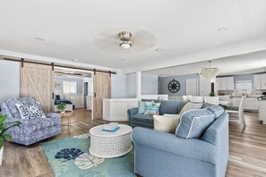 A spacious living area with a sofa, armchair, and coffee table, a kitchen in the background, and a sliding barn door.