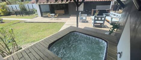 A hot tub on a wooden deck with a view of a house and a grassy yard.