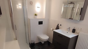 A modern bathroom with a glass shower enclosure, a toilet, a sink with a mirror, and a radiator. - Cozy 2 room apartment for 2-4 persons between Kiel-City and the beaches (Schönkirchen)