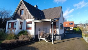 A two-story house with a sloped roof, a front porch, and a paved driveway. - Cozy 2 room apartment for 2-4 persons between Kiel-City and the beaches (Schönkirchen)