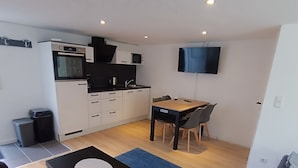 A compact living space with a kitchenette, a dining area, and a flat-screen TV mounted on the wall. - Cozy 2 room apartment for 2-4 persons between Kiel-City and the beaches (Schönkirchen)
