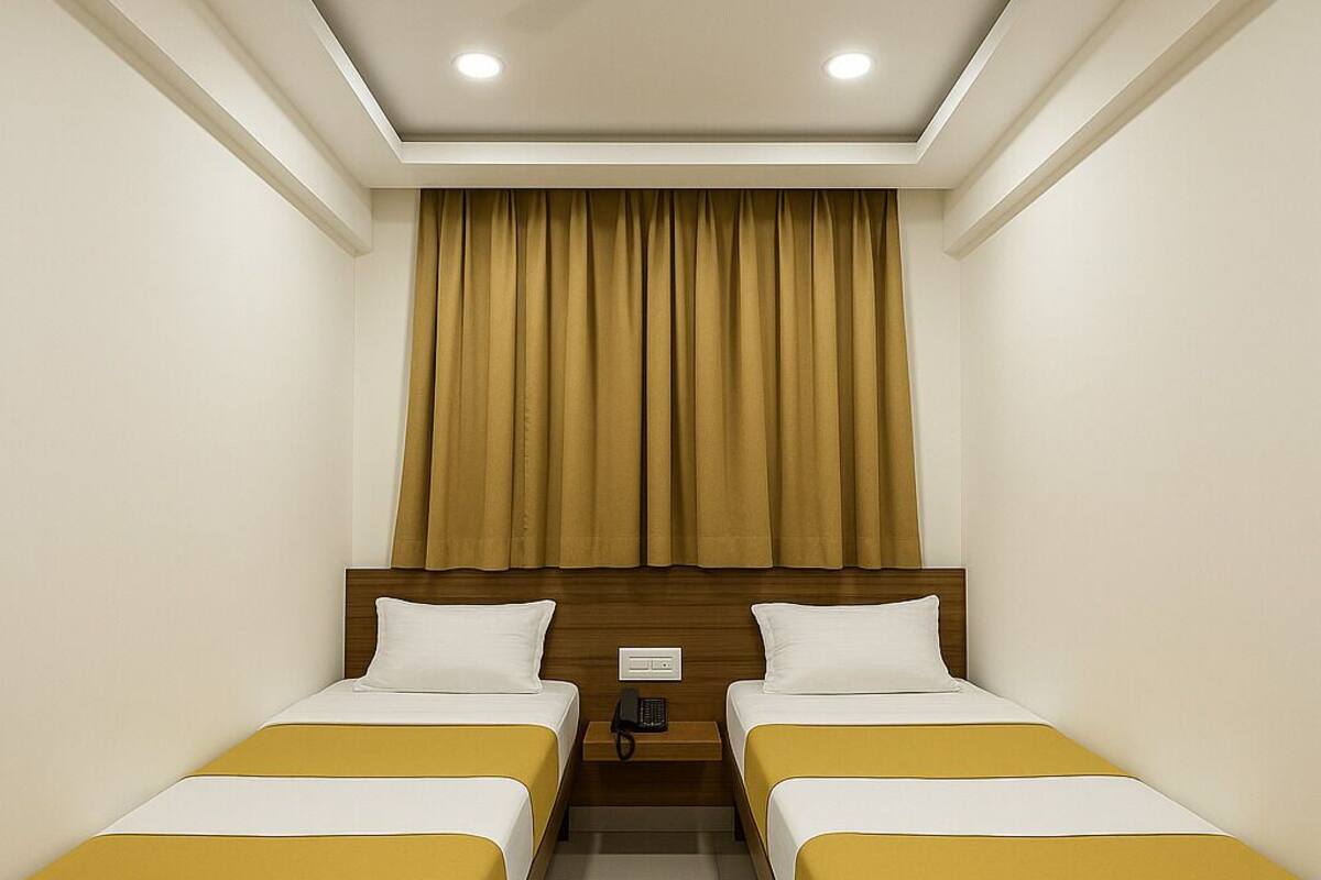 Quarto de hotel com duas camas, cabeceira de madeira, luminária no teto e cortina.