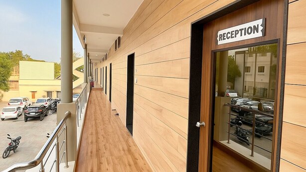Un pasillo con recepción, paneles de madera y vistas al exterior, donde se ven coches estacionados y una motocicleta.