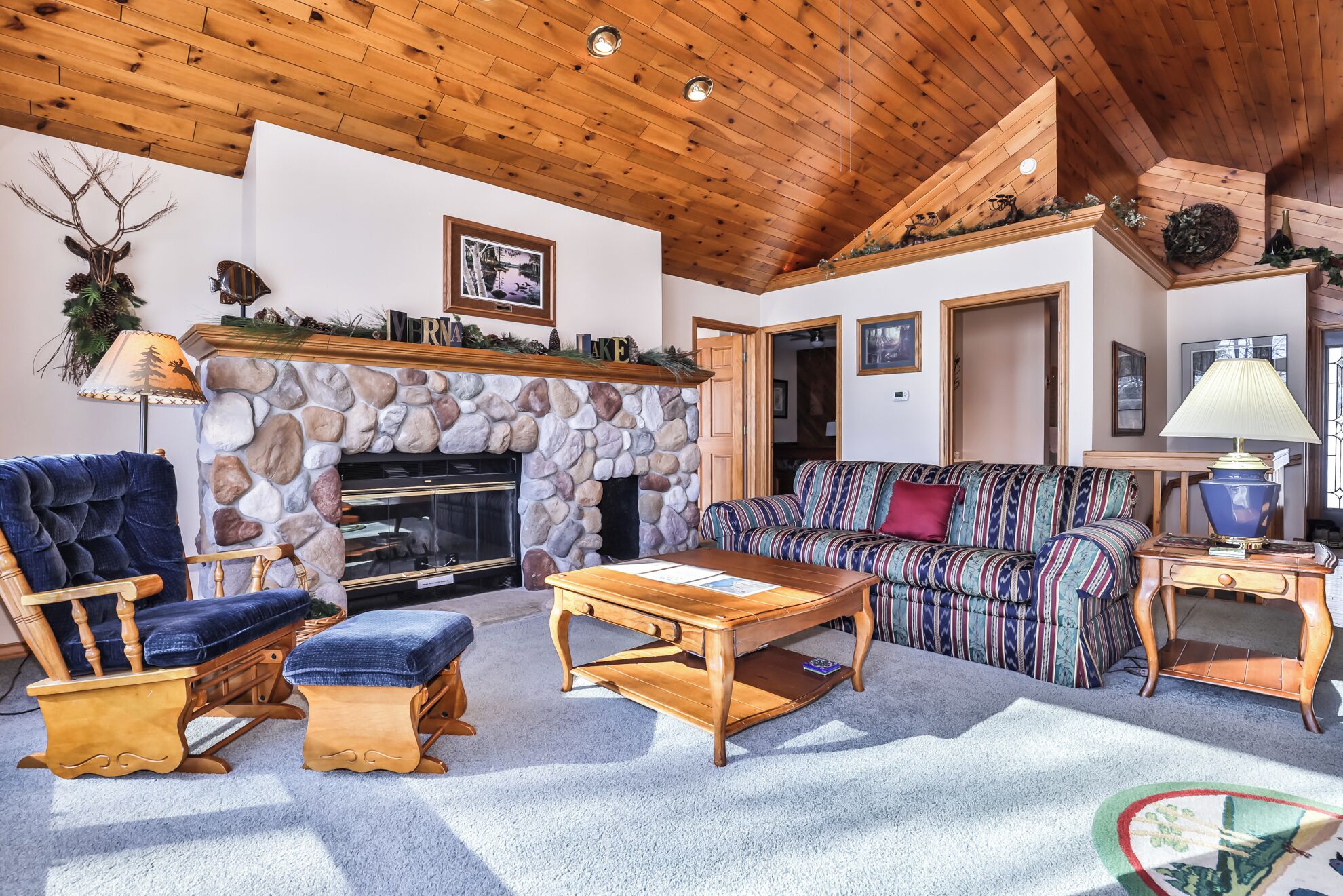A cozy living room with a stone fireplace, wooden ceiling, and a sofa.