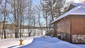 Una cabaña de madera con base de piedra, rodeada de nieve y árboles.
