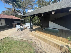 Una terraza de madera con un jacuzzi, mobiliario exterior y una zona de barbacoa.