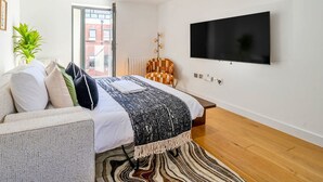 Et moderne soveværelse med seng, fjernsyn, en plante og udsigt ud.