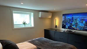 A modern bedroom with a bed, a TV mounted on the wall, a window with a view of the outside, and a ceiling light.