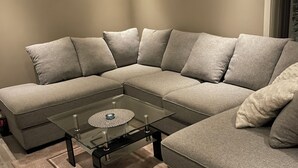 A modern living room with a sectional sofa, a glass coffee table, and a wooden floor.