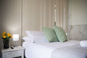 A hotel room with a bed, white bedding, a nightstand with a lamp and a vase of flowers, and a marble wall.