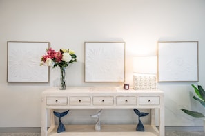 A wooden console table with four drawers, a vase with flowers, and three framed wall art pieces. - 23B Airlie View (Airlie Beach)