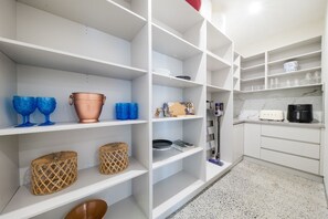 Eine Küche mit weißen Schränken, einer Arbeitsplatte mit Toaster und Regalen, auf denen verschiedene Gegenstände wie Körbe und ein Kupfertopf stehen.
