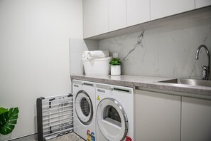 A laundry area with a washing machine, a drying rack, and a sink. - 23B Airlie View (Airlie Beach)
