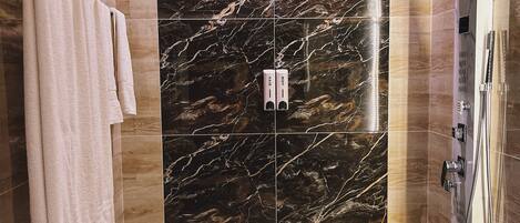 A modern bathroom with a marble wall, a shower with a handheld showerhead, and two towels on a rack.