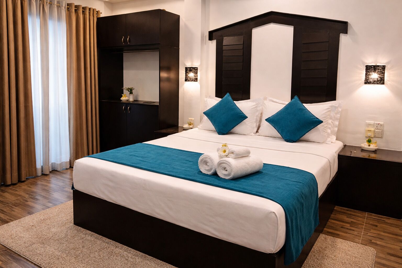A hotel room with a bed, a nightstand, a wardrobe, and a wall-mounted light fixture.