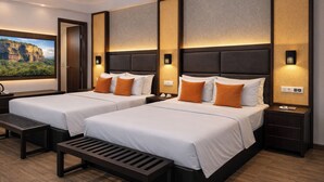 Ein Hotelzimmer mit zwei Betten, einer Bank, einem Nachttisch, einem an der Wand montierten Fernseher und einem großen Fenster mit Blick auf die Berge.